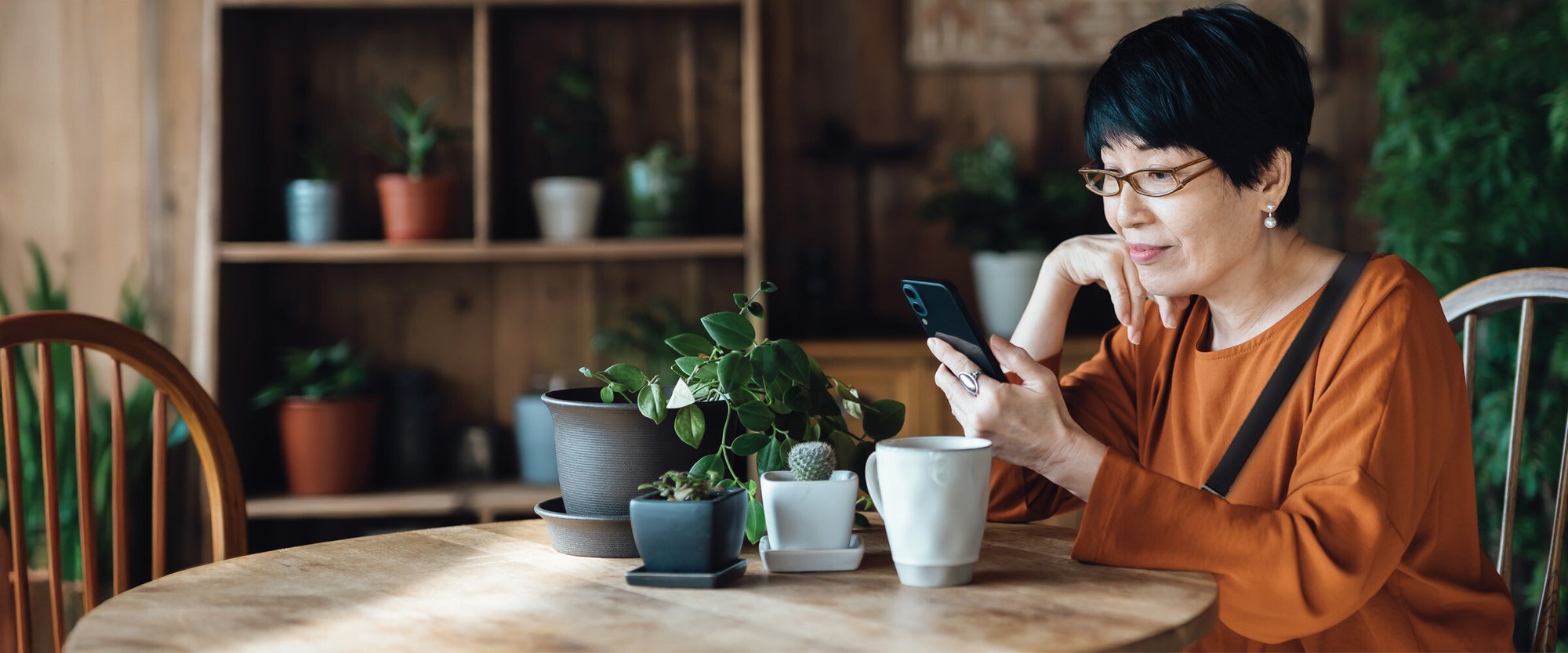 A woman wearing glasses sitting down at a table while looking at her phone